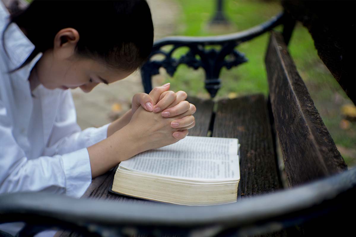 lady praying with bible on a park bench
