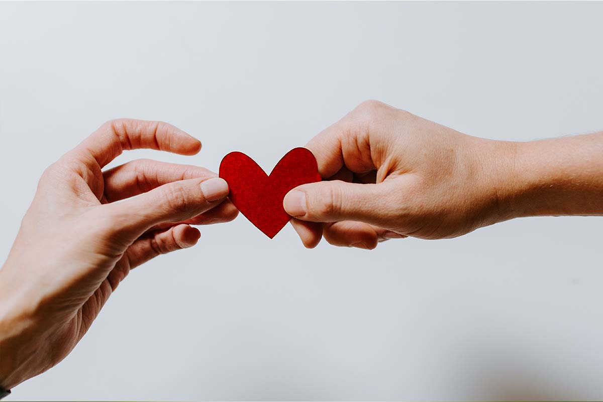 Hand passing a red heart to another hand