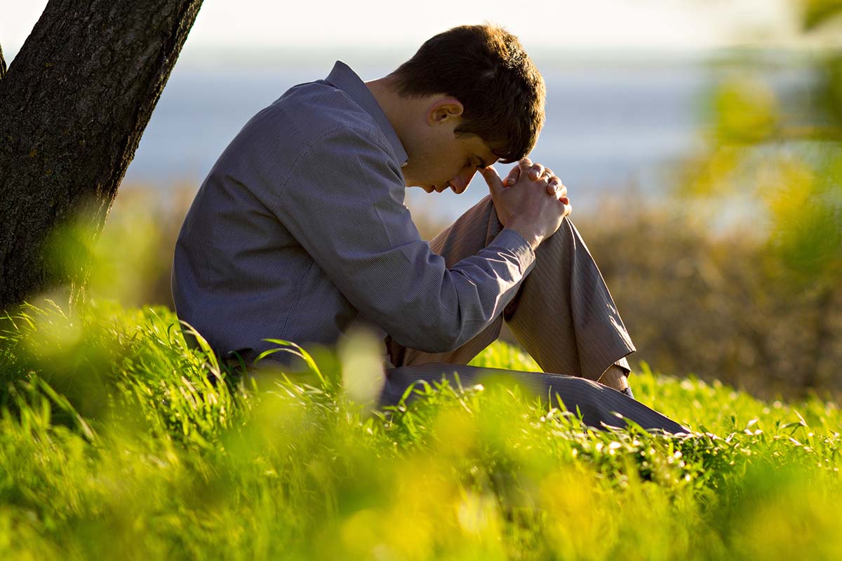 young man praying to God in the nature bowing his head to his knees, concept religion